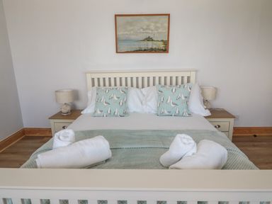 A bedroom with a bed with seagull patterned pillows towels on a green blanket and lamps on bedside tables at 24 Hauxley Links in Low Hauxley near Amble