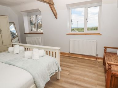 A bedroom with a bed and rolled towels a wardrobe a mirror two windows and a wooden bench at 24 Hauxley Links in Low Hauxley near Amble