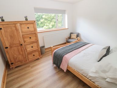 A bedroom with a wooden bed a wooden wardrobe and a gray armchair by the window at 24 Hauxley Links in Low Hauxley near Amble