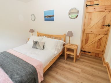 A bedroom with a wooden bed frame with white bedding a bedside table with a lamp and a wooden door at 24 Hauxley Links in Low Hauxley near Amble