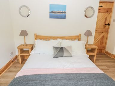 A bedroom with a wooden bed frame bedside tables with lamps and a door at 24 Hauxley Links in Low Hauxley near Amble