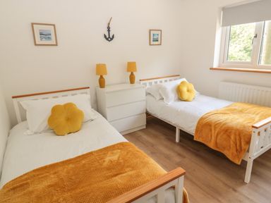 A bedroom with two single beds with yellow blankets and pillows a white dresser with two yellow lamps and a window at 24 Hauxley Links in Low Hauxley near Amble