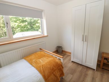 A bedroom with a single bed with a yellow blanket a white wardrobe a window and a small wooden shelf at 24 Hauxley Links in Low Hauxley near Amble