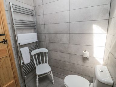 A bathroom with a white toilet a white wooden chair a chrome towel rack with towels and a wooden door at 24 Hauxley Links in Low Hauxley near Amble