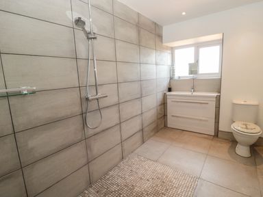 A bathroom with a shower area a sink under a window and a toilet with an anchor design on the seat cover at 24 Hauxley Links in Low Hauxley near Amble