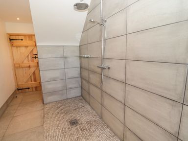 A walk in shower with tiled walls and floor and a wooden door in a bathroom at 24 Hauxley Links in Low Hauxley near Amble
