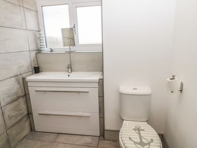 A bathroom with a sink vanity unit under a window and a toilet with an anchor design on the lid at 24 Hauxley Links in Low Hauxley near Amble