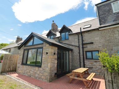 An exterior view of a stone house with a small patio and wooden picnic table at 24 Hauxley Links in Low Hauxley near Amble