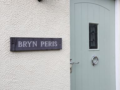 A wall with a sign reading Bryn Peris next to a light blue door with a small window at Bryn Peris in Moelfre