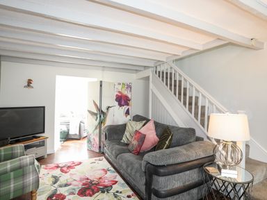 A living room with a gray sofa and pillows a floral rug a green plaid armchair a TV on a stand and a lamp on a side table at Bryn Peris in Moelfre