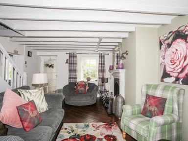 A living room with sofas armchairs a fireplace and floral rug at Bryn Peris in Moelfre