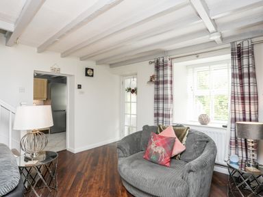 A living room with two grey armchairs with pillows beside a window with curtains and a door visible Bryn Peris in Moelfre