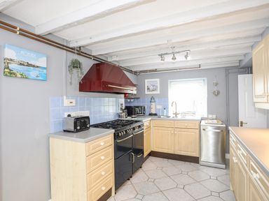 A kitchen with light wood cabinets a black stove a silver dishwasher and a window at Bryn Peris in Moelfre