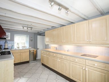 A kitchen with wooden cabinets tiled floor and a stainless steel dishwasher at Bryn Peris in Moelfre