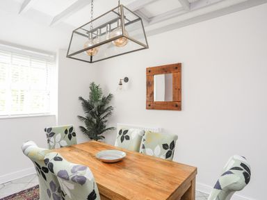 A dining room with a wooden table and floral patterned chairs a mirror on the wall and a plant near the window at Bryn Peris in Moelfre