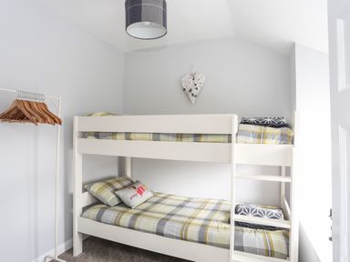 A bedroom with a white bunk bed and a clothes rack with hangers at Bryn Peris in Moelfre