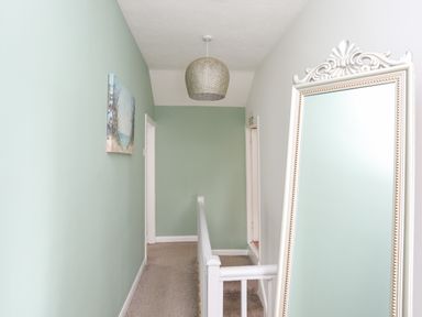 A hallway with green and white walls a large upright mirror a ceiling light and a framed picture at Bryn Peris in Moelfre