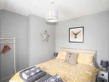 A bedroom with a double bed covered in yellow patterned bedding and a pillow with a rabbit design at Bryn Peris in Moelfre