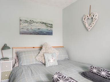 A bed with checkered bedding and two pillows next to a bedside table with a lamp and a wall painting above at Bryn Peris in Moelfre