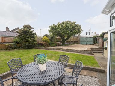 A garden with a black metal table and chairs a potted plant green grass and trees at Bryn Peris in Moelfre