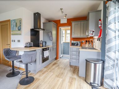 A kitchen with grey cabinets a breakfast bar with two stools and an orange wall at Bryn Hyfryd in Harlech