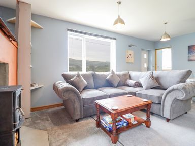 A living room with a gray sectional sofa a wooden coffee table and a wood stove at Bryn Hyfryd in Harlech