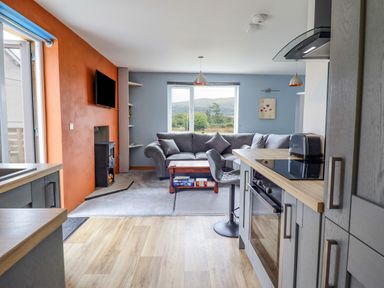 A living room and kitchen area with a gray sofa a wooden coffee table and kitchen cabinets at Bryn Hyfryd in Harlech