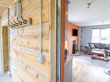A wooden hallway with hooks beside a living room with gray sofas and a wooden coffee table at Bryn Hyfryd in Harlech