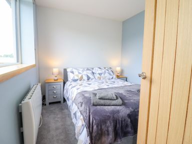 A bedroom with a bed covered in geometric patterned bedding and two bedside tables with lamps at Bryn Hyfryd in Harlech