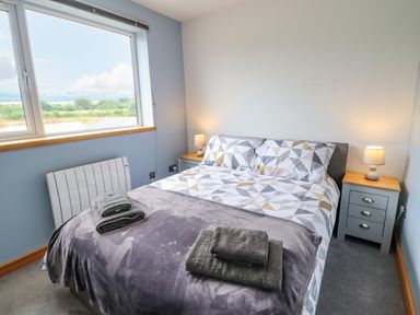 A bedroom with a double bed bedside tables lamps and folded towels on the bed at Bryn Hyfryd Harlech