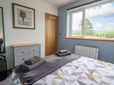 A bedroom with a bed folded towels a chest of drawers and a window showing outdoor scenery at Bryn Hyfryd in Harlech