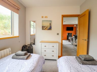A bedroom with two beds and towels on them a dresser a mirror and a door opening to a living room at Bryn Hyfryd in Harlech