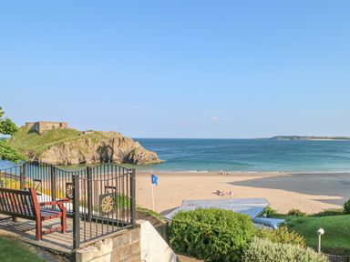 A sandy beach with a few people and a small rocky island with a building at Cambrie Tenby