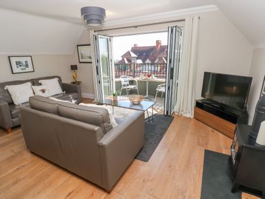 A living room with two brown sofas a glass coffee table a television and an open door leading to a balcony at Cambrie in Tenby