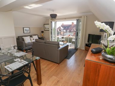 A living room with a glass dining table set a grey sofa and a balcony at Cambrie in Tenby