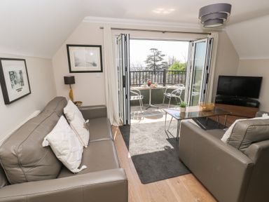 A living room with leather sofas a glass coffee table a television and balcony doors open to an outdoor seating area at Cambrie in Tenby