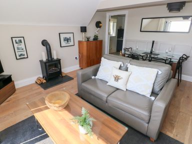 A living room with a leather sofa, wooden coffee table, wood burning stove and dining table at Cambrie in Tenby