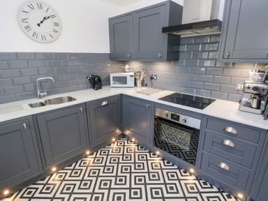 A kitchen with grey cabinets white countertops a built-in oven stove microwave and patterned floor at Cambrie in Tenby
