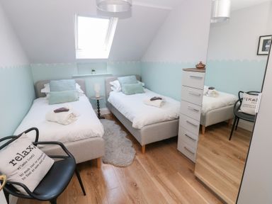 A bedroom with two single beds a bedside table a black chair with a cushion and a tall cupboard with a mirror at Cambrie in Tenby