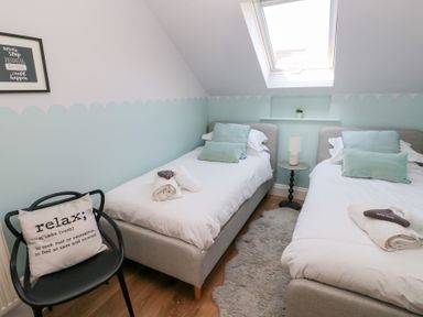 A bedroom with two single beds a black chair with a cushion a small round table with a lamp and a skylight window at Cambrie in Tenby