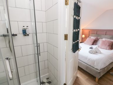 A bedroom with a bed and pillows next to a bathroom with a glass shower at Cambrie in Tenby