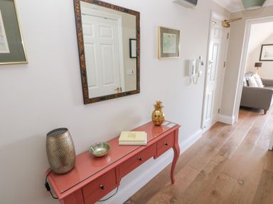A hallway with wooden floor a red console table with decorative items and a mirror on the wall at Cambrie in Tenby