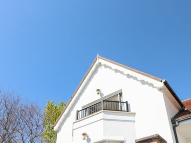 Exterior view of a white house with a small balcony and a sloped roof under a clear blue sky at Cambrie in Tenby