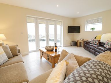 A living room with two sofas a wooden coffee table a wall mounted TV and glass doors at Hen Dy Bryn Mawndy Melin y Wig near Corwen