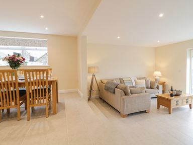 An open dining and living area with wooden dining table and chairs on the left and beige sofas with wooden coffee table on the right at Hen Dy Bryn Mawndy Melin y Wig near Corwen