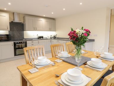 A kitchen with light cabinets and black stove and a dining table set with white dishes and flowers at Hen Dy Bryn Mawndy Melin y Wig near Corwen