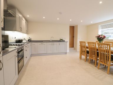 A kitchen with gray cabinets and a dining table with wooden chairs and flowers at Hen Dy Bryn Mawndy Melin y Wig near Corwen