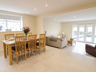 A dining table with six wooden chairs and flowers in a vase next to a seating area with sofas and a coffee table in a living room at Hen Dy Bryn Mawndy Melin y Wig near Corwen