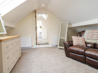 An attic room with a leather sofa a dresser a mirror and an open door leading to a bathroom at Hen Dy Bryn Mawndy Melin y Wig near Corwen