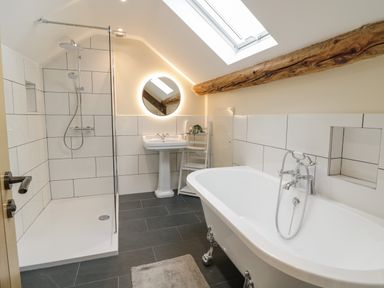 A bathroom with a bathtub a shower a sink a round mirror and a skylight at Hen Dy Bryn Mawndy Melin y Wig near Corwen
